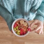 person holding white ceramic bowl with red and yellow beans